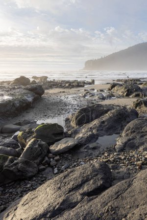 Téléchargez les photos : Une plage rocheuse avec un ciel nuageux en arrière-plan. Les rochers sont éparpillés sur toute la plage, et l'eau est calme. Scène paisible et sereine, avec les rochers - en image libre de droit