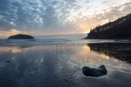 Téléchargez les photos : Une plage rocheuse avec une petite île au loin. Le ciel est nuageux et le soleil se couche - en image libre de droit