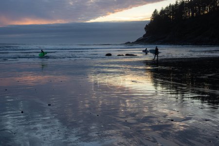 Un grupo de personas están en una playa, con la puesta de sol en el fondo. La escena es tranquila y serena, ya que la gente disfruta de su tiempo en el agua