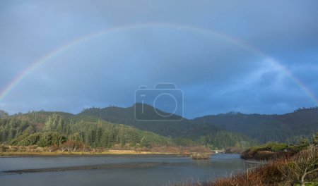 Photo for A rainbow is seen over a body of water. The sky is cloudy and the water is calm - Royalty Free Image