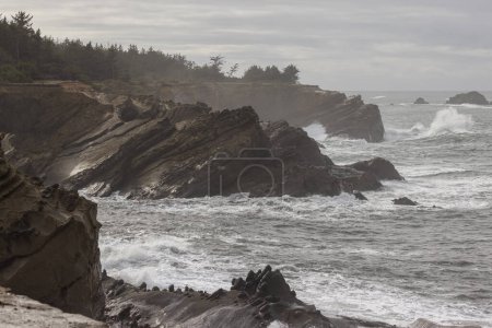 Foto de Una costa rocosa con un gran cuerpo de agua en el fondo. Las olas se estrellan contra las rocas, creando una escena poderosa y dinámica. La escena es de fuerza y resiliencia - Imagen libre de derechos