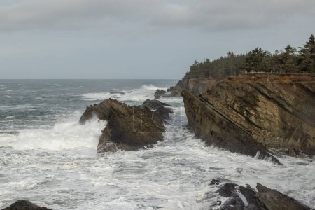 Foto de El océano es áspero y las rocas son dentadas. Las olas se estrellan contra las rocas, creando una escena poderosa y dinámica. La escena es de fuerza y resiliencia - Imagen libre de derechos
