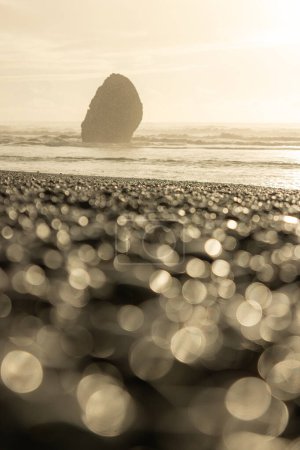 Foto de Una playa rocosa con una gran roca en primer plano. La roca está rodeada por un fondo borroso, dando a la imagen una cualidad soñadora y etérea. El agua en el fondo es tranquila - Imagen libre de derechos