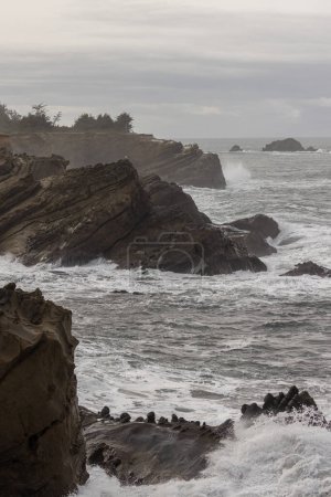 Téléchargez les photos : Un rivage rocheux avec un grand plan d'eau en arrière-plan. Les vagues s'écrasent contre les rochers, créant une scène puissante et dynamique. Scène est une scène de force et de résilience - en image libre de droit