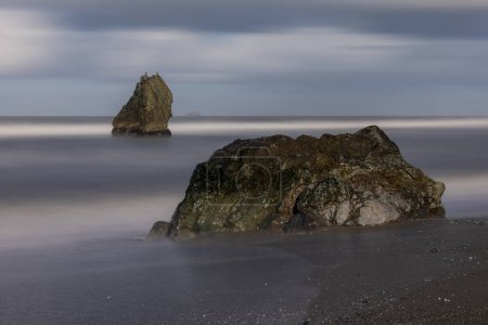 Photo for A rock is on the beach next to the water. The water is calm and the sky is cloudy - Royalty Free Image