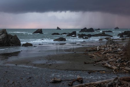 Foto de Una playa rocosa con un cielo tormentoso en el fondo. El cielo está oscuro y nublado, y las olas se estrellan contra las rocas. La playa está llena de rocas y escombros, y el agua está picada - Imagen libre de derechos