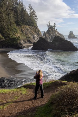 Téléchargez les photos : Une femme tenant un petit chien profitant du beau paysage de Secret Beach, Oregon. - en image libre de droit
