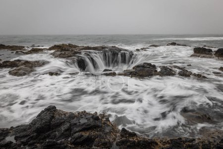 Photo for A rocky feature in the central Oregon Coast that looks like the ocean is draining thru a well - Royalty Free Image