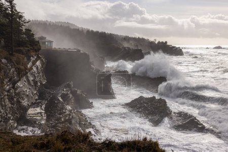 Foto de El océano es áspero y las olas se estrellan contra las rocas. El cielo está nublado y el sol brilla a través de las nubes - Imagen libre de derechos
