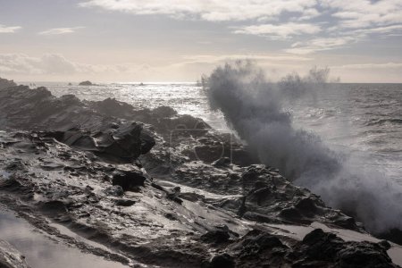 Téléchargez les photos : L'océan est rude et les vagues s'écrasent contre les rochers. Le ciel est nuageux et le soleil brille à travers les nuages. Scène intense et puissante - en image libre de droit