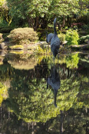 Téléchargez les photos : Une statue d'oiseau se tient dans un étang avec son reflet dans l'eau. Concept de tranquillité et de tranquillité, car l'oiseau et son reflet semblent être en harmonie avec l'environnement naturel - en image libre de droit