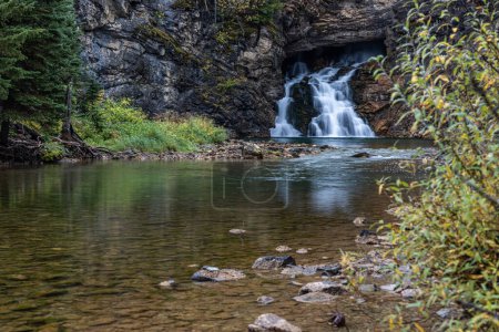 Photo for A waterfall is flowing into a river. The water is clear and calm. The rocks around the river are jagged and rough. The trees surrounding the river are tall and green. The scene is peaceful and serene - Royalty Free Image