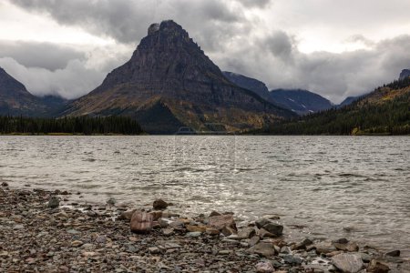 Téléchargez les photos : Une chaîne de montagnes est en arrière-plan avec un lac au premier plan. Le ciel est nuageux et l'eau calme - en image libre de droit