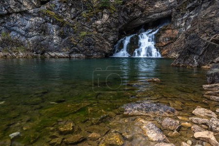 Photo for A waterfall is flowing into a small pool of water. The water is clear and calm, and the rocks around the pool are scattered. The scene is peaceful and serene - Royalty Free Image