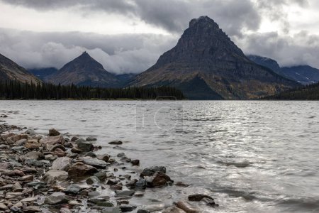 Téléchargez les photos : Une chaîne de montagnes est en arrière-plan avec un lac en face de lui. Le lac est calme et le ciel est nuageux - en image libre de droit
