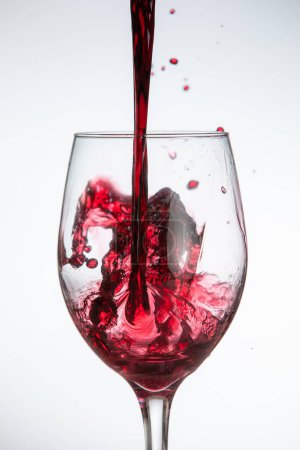 Foto de Una copa de vino tinto se vierte en una copa, y el vino está salpicando en la copa. - Imagen libre de derechos