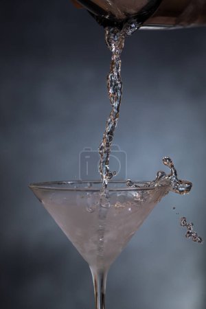 Photo for Action shot of pouring chilled vodka into a martini glass over a blueish background. - Royalty Free Image