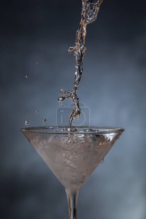 Téléchargez les photos : Plan d'action consistant à verser du rhum réfrigéré dans un verre de martini sur un fond bleu. - en image libre de droit