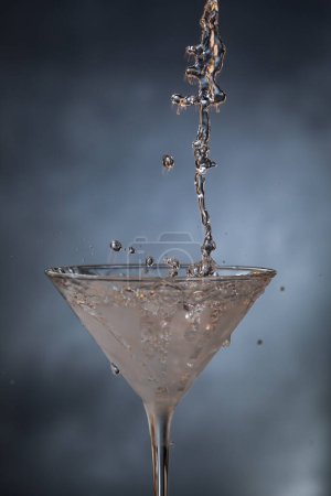 Foto de Toma de acción de verter tequila de plata refrigerada en un vaso de martini sobre un fondo azulado. - Imagen libre de derechos