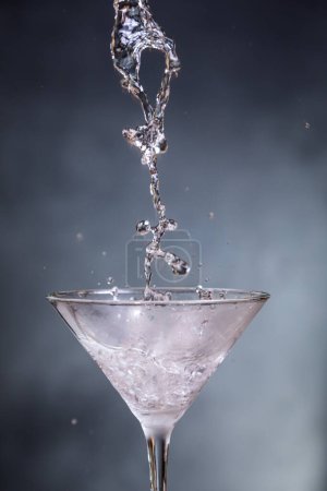 Foto de Toma de acción de verter vodka refrigerado en un vaso de martini sobre un fondo azulado. - Imagen libre de derechos