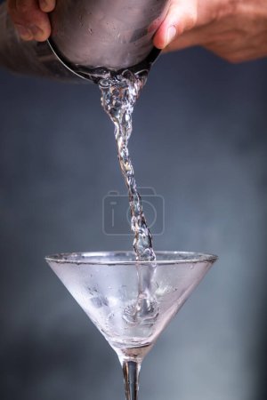 Téléchargez les photos : Plan d'action consistant à verser du gin réfrigéré dans un verre de martini sur un fond bleu. - en image libre de droit