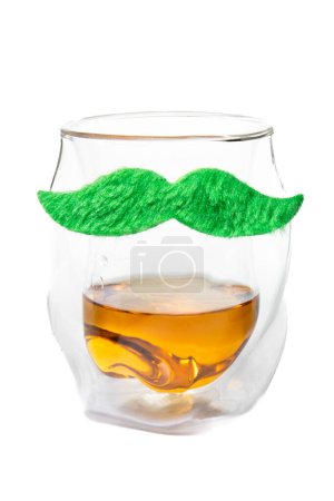 Téléchargez les photos : Un verre avec une moustache dessus. La moustache est verte et est faite de fils. Le verre est rempli d'une boisson - en image libre de droit