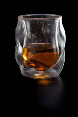 Photo for A glass of liquor is sitting on a table. The glass is half full and the liquor is brown - Royalty Free Image