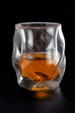 Téléchargez les photos : Un verre de liqueur dans un verre avec une forme incurvée. Le verre est à moitié plein et la liqueur est brune - en image libre de droit