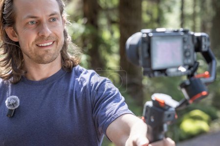 Photo for Content creator using a camera gimbal to film in nature with a blurred forest in the background - Royalty Free Image