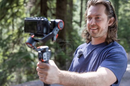 Photo for Content creator using a camera gimbal to film in nature with a blurred forest in the background - Royalty Free Image