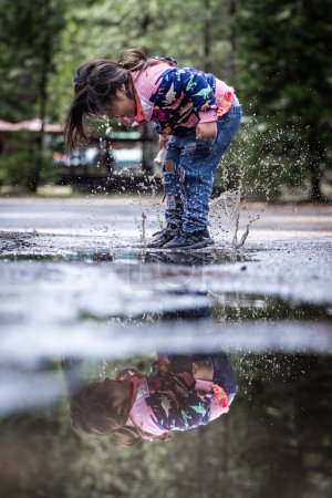 Téléchargez les photos : Une petite fille joue sous la pluie et éclabousse l'eau. L'image a une humeur ludique et joyeuse - en image libre de droit
