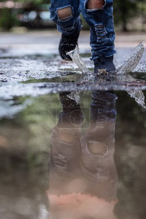 Téléchargez les photos : Une personne marche sous la pluie avec les pieds dans l'eau. Le reflet de la personne et de ses chaussures peut être vu dans l'eau - en image libre de droit