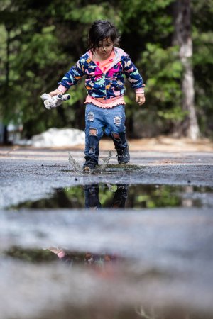 Photo for A young girl is playing in the rain, splashing in puddles. The scene is playful and joyful, with the girl enjoying the moment and the wet environment - Royalty Free Image