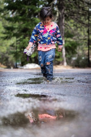 Foto de Una joven está caminando a través de un charco de agua, sosteniendo un juguete en su mano. La escena es juguetona y alegre, con la chica disfrutando de su tiempo al aire libre a pesar de las condiciones húmedas - Imagen libre de derechos