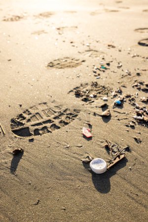 Téléchargez les photos : Une plage avec des ordures sur le sable et une empreinte dans le sable. Scène est triste et sale - en image libre de droit