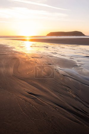 Photo for A beach with a small island in the distance. The sun is setting and the sky is a mix of orange and pink - Royalty Free Image