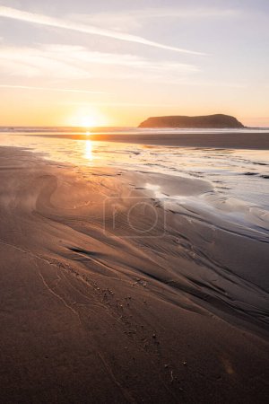Téléchargez les photos : Une plage avec une petite île au loin. Le soleil se couche et le ciel est un mélange d'orange et de rose - en image libre de droit