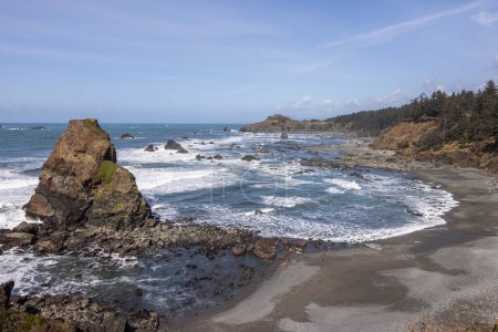 Una playa rocosa con una gran roca en primer plano y un cuerpo de agua en el fondo. La escena es tranquila y pacífica, con las olas golpeando suavemente en la orilla