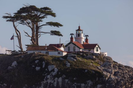 Photo for A lighthouse sits on a rocky hillside. The lighthouse is white and red, and it is surrounded by a lush green hillside. The scene is peaceful and serene. Battery Point Lighthouse, California. - Royalty Free Image