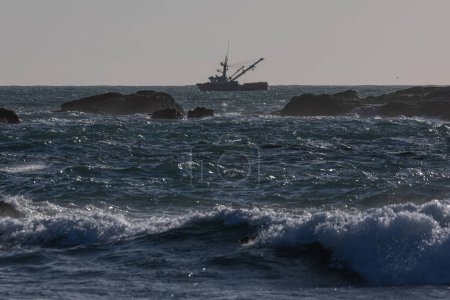 Foto de Un barco está en el agua con una red de pesca. El agua está agitada y el cielo nublado - Imagen libre de derechos
