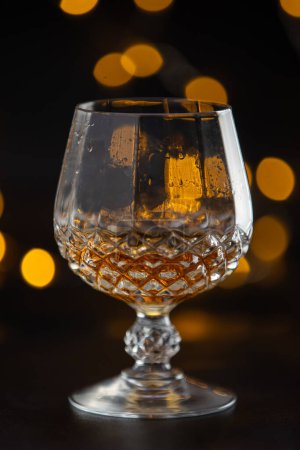 Photo for A glass of alcohol is sitting on a table. The glass is half full and has a yellowish tint. The image has a moody and mysterious feel to it, as the focus is on the glass and the liquid inside it - Royalty Free Image