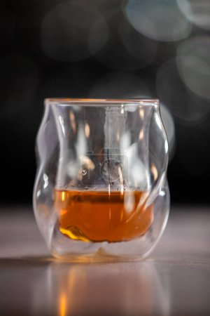 Photo for A glass of liquor is sitting on a table. The glass is half full and the liquid inside is brown. Concept of relaxation and enjoyment, as the glass of liquor is often associated with socializing - Royalty Free Image