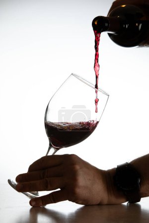 Téléchargez les photos : Action shot verser du vin rouge dans un verre sur un fond blanc - en image libre de droit