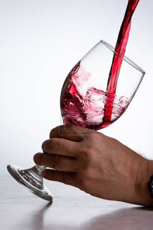 Téléchargez les photos : Action shot verser du vin rouge dans un verre sur un fond blanc - en image libre de droit