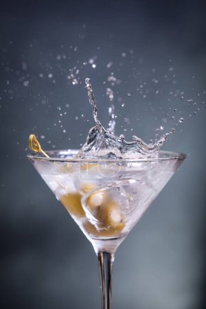 Foto de Primer plano de una toma de acción de aceitunas verdes rellenas con queso bleu caído en un martini vodka - Imagen libre de derechos