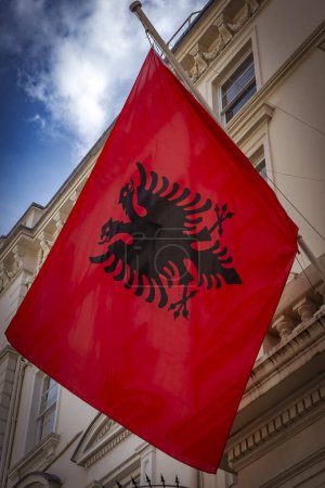 Albanian flag hanging outside grand residence under cloudy sky