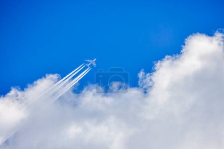 Photo for A plane flying through a blue cloudy sky leaving white traces behind it - Royalty Free Image