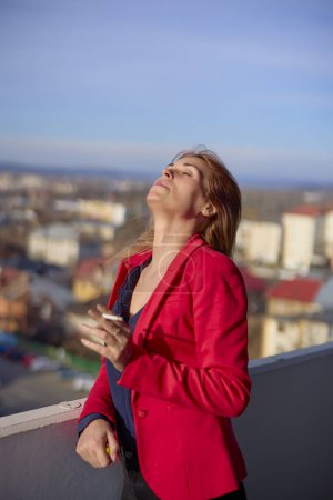Foto de Una mujer en el balcón fumando en un día soleado. - Imagen libre de derechos