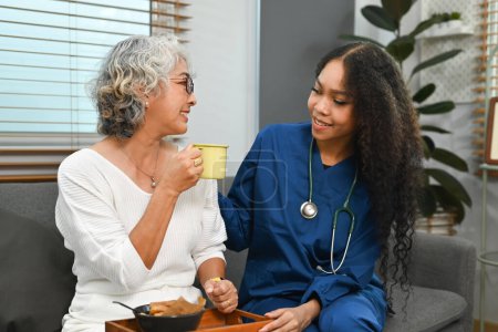 Foto de Visitante positiva de salud femenina hablando, dando consejos a las mujeres mayores durante la visita domiciliaria. Concepto de salud de adultos mayores. - Imagen libre de derechos