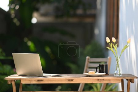 Photo for Laptop computer, cup of coffee, notebook and flower pot on wooden table at outdoor. - Royalty Free Image